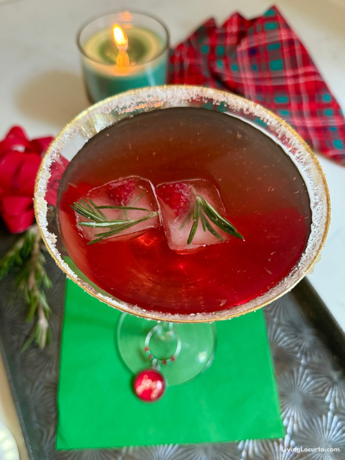 Close up photo of a Cranberry Martini with fruit-filled rosemary ice cubes. Green napkin and christmas themed drink.
