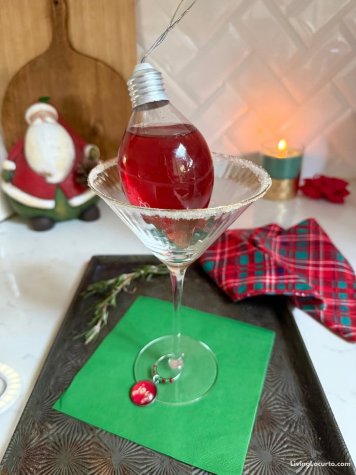 Christmas Cranberry Martini recipe with a fun holiday twist! Christmas ornament drink holder, sugared rims, and fruit-filled rosemary ice cubes in a martini glass.
