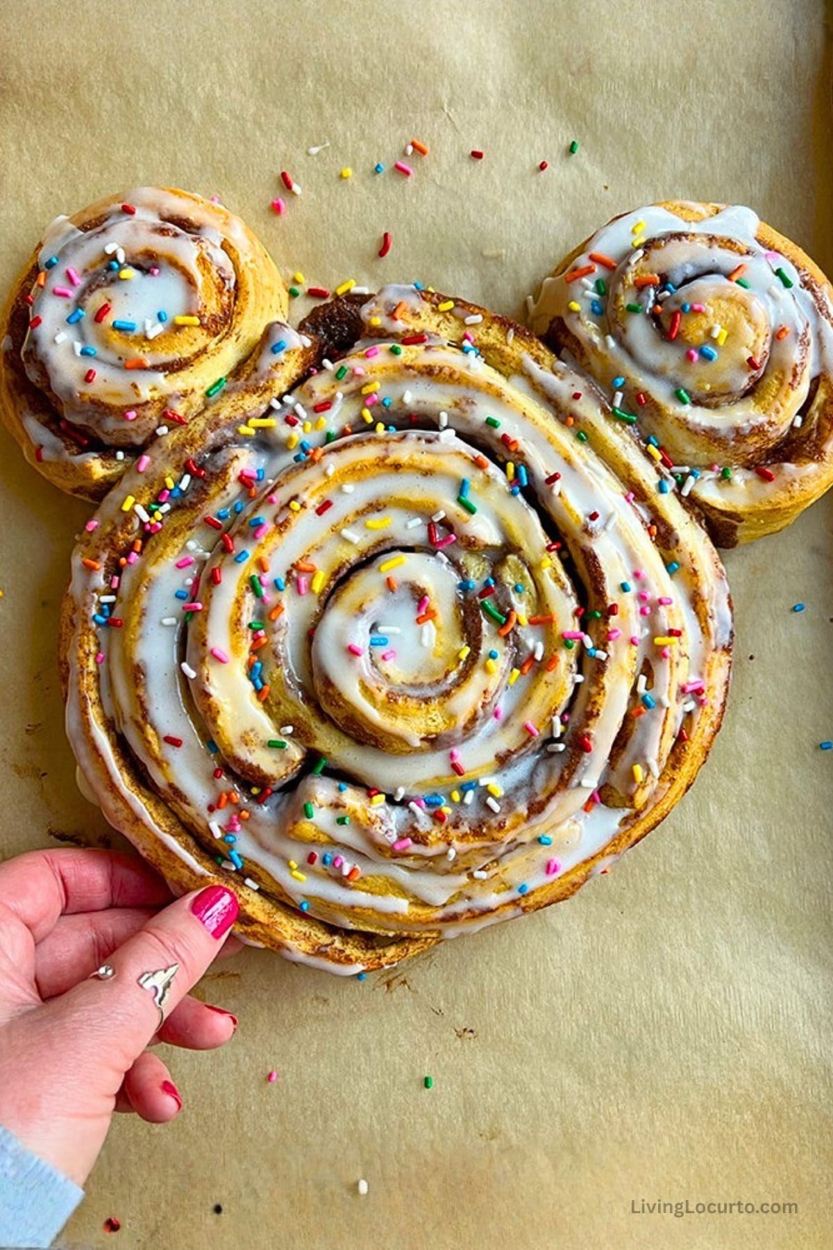 Disney Inspired Giant Mickey Shaped Cinnamon Roll with colorful rainbow sprinkles on parchment paper.