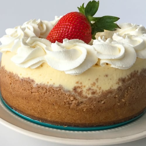Copycat Cheesecake Factory Cheesecake 13 round cheesecake cake with whipped cream and a large strawberry in the center