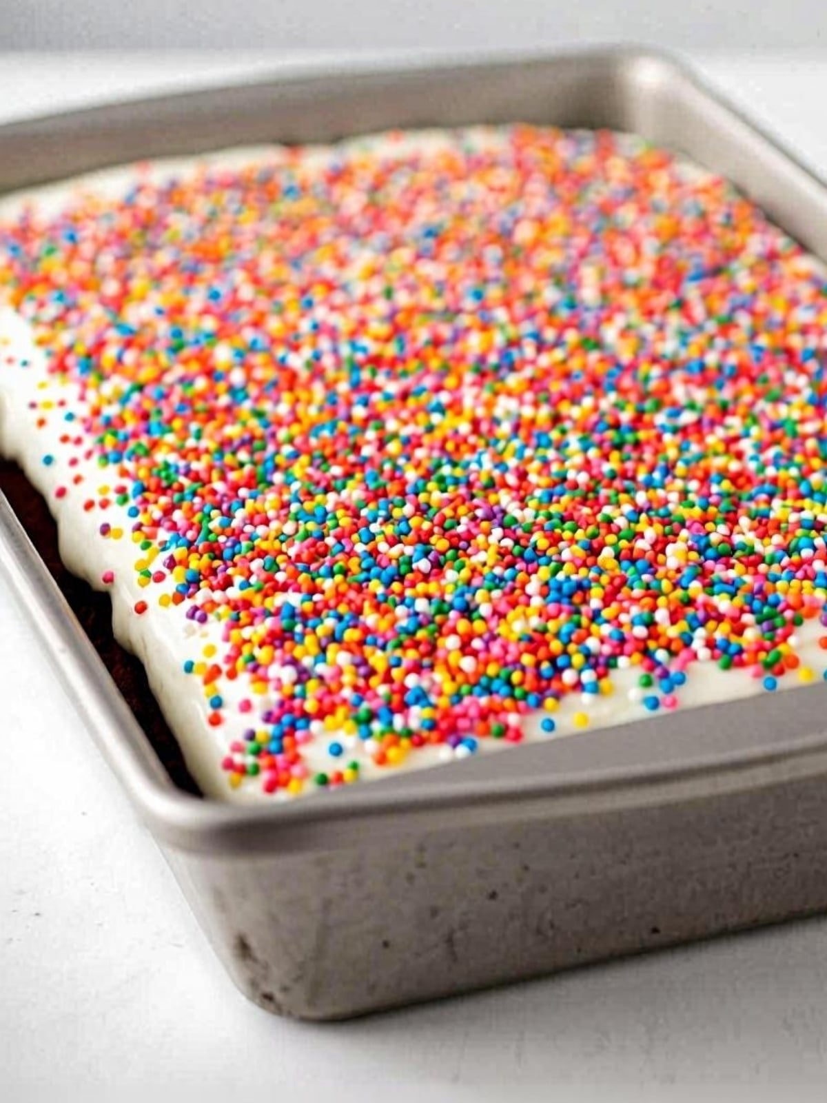 A baking pan full of Dot Cake brownies with thick coat of vanilla frosting and rainbow sprinkles.