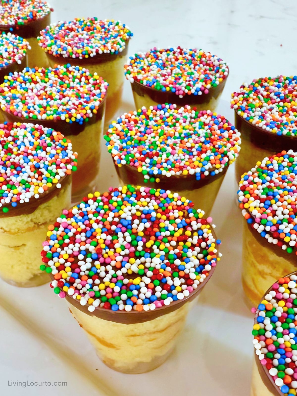 Mini Dot Cakes (Dot Shots) 1 Close up Mini Dot Cake shots with rainbow sprinkles and gold spoons on a white party platter.