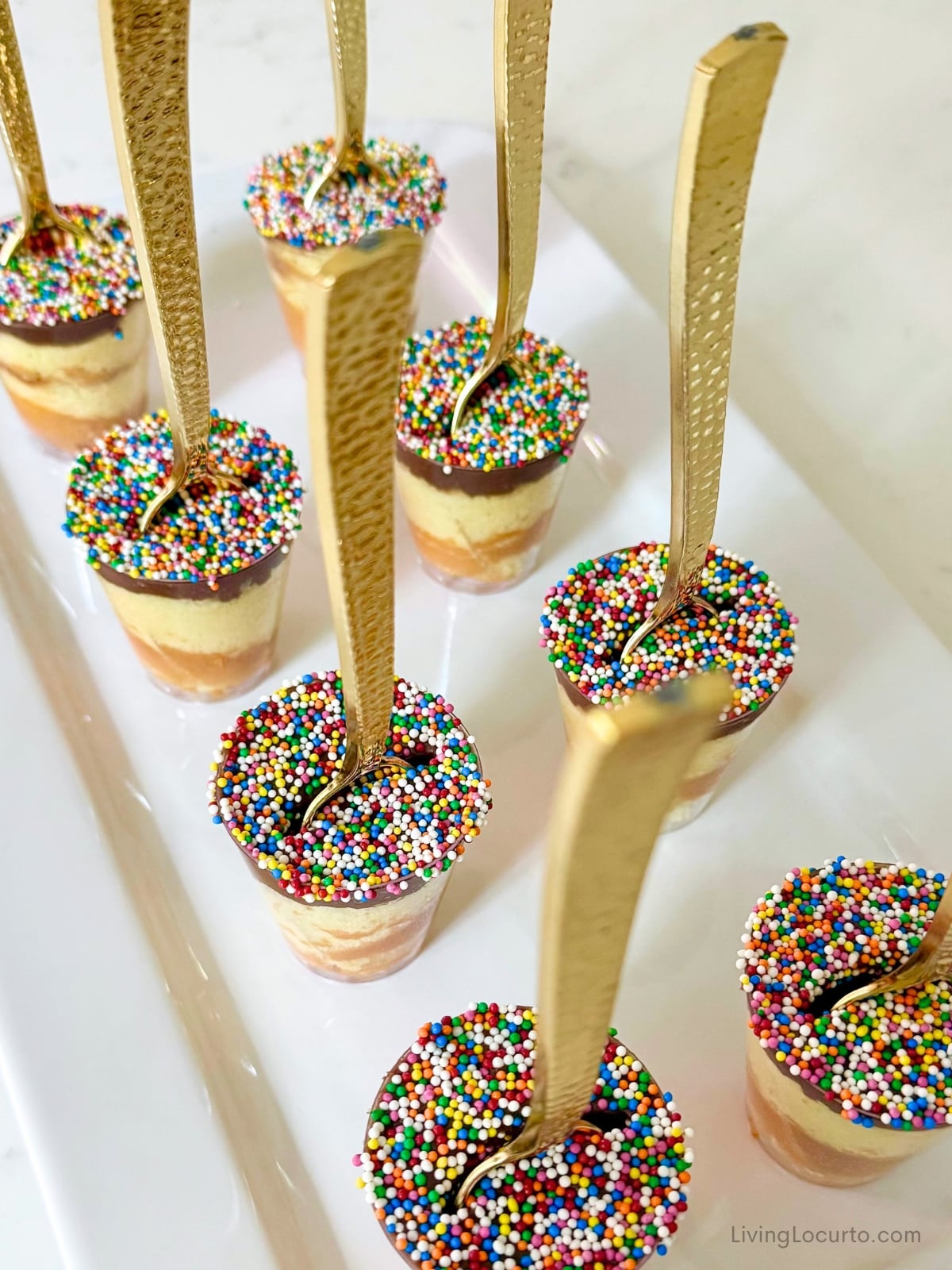 Mini Dot Cakes (Dot Shots) 8 Mini Dot Cake shots with rainbow sprinkles and gold spoons on a white party platter.