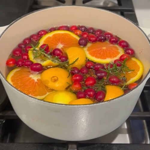 Cranberry holiday simmer pot with orange slices, spices, and rosemary simmering on a stove.