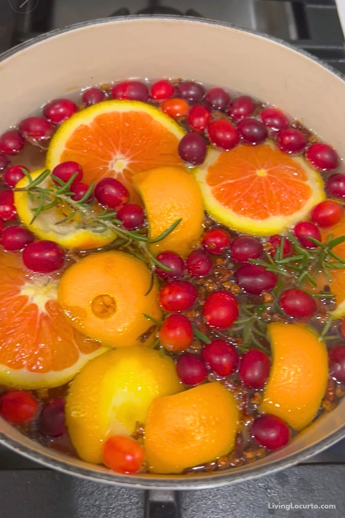 Cranberry holiday simmer pot with orange slices, spices, and rosemary simmering on a stove.